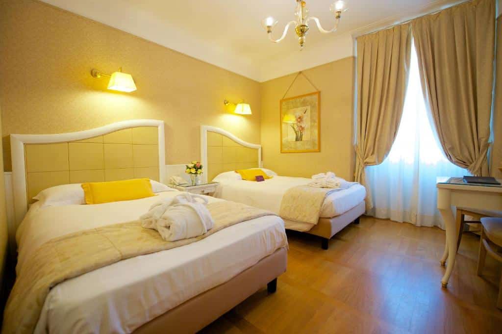 Quarto do Hotel Mercure Milano Centro com uma cama de casal, uma de solteiro, uma janela com cortinas, há luminárias presas na parede perto das camas, assim como um lustre no centro do quarto, para representar hotéis Mercure em Milão