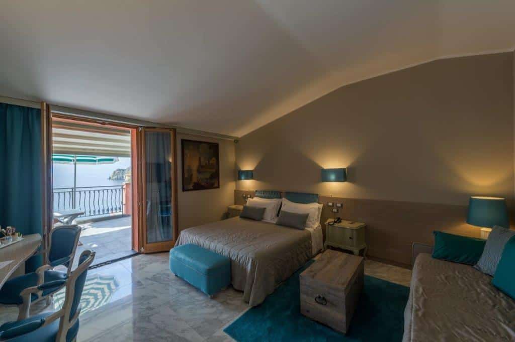 Quarto com duas camas, móveis e tapete azul claro, quadro na parede e uma porta enorme de vidro com acesso para a varanda.