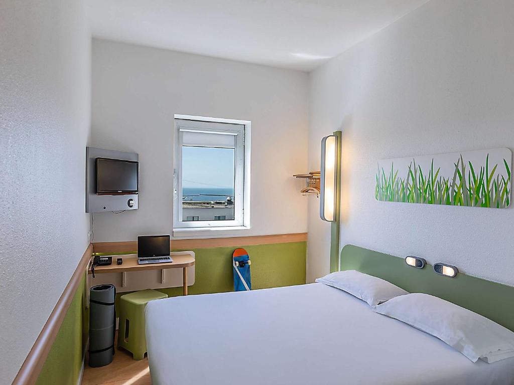 Quarto do Hotel ibis Budget Porto Gaia com cama de casal do lado direito a imagem, do lado esquerdo da cama uma mesa de trabalho e em cima uma TV presa na parede. Representa hotéis Mercure no Porto.