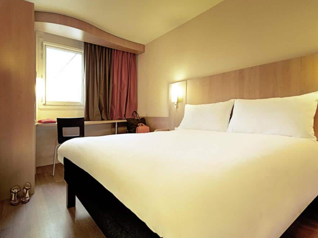 Quarto do ibis Porto Centro São Bento com cama de casal do lado direito e do lado esquerdo da cama uma mesa de trabalho. Representa hotéis Mercure no Porto.