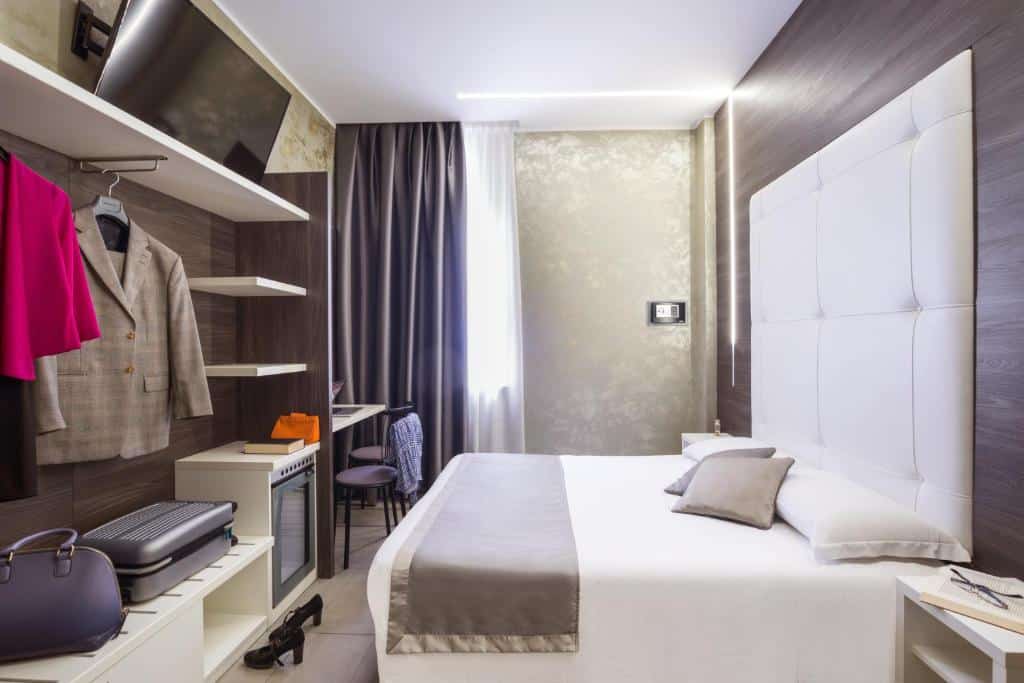 Quarto do Ibis Styles Milano Centro com uma janela com cortinas, uma cama de casal com uma cabeceira estofada, um armário de conceito aberto, uma televisão e uma mesa de escritório com uma cadeira