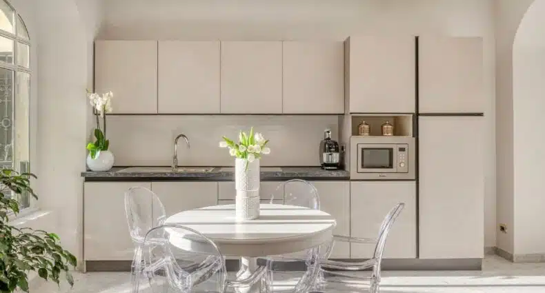 Cozinha do Imperiale Suites Milano com uma mesa redonda com cadeiras transparentes, há um vaso de plantas sob a mesa, para representar airbnb em Milão