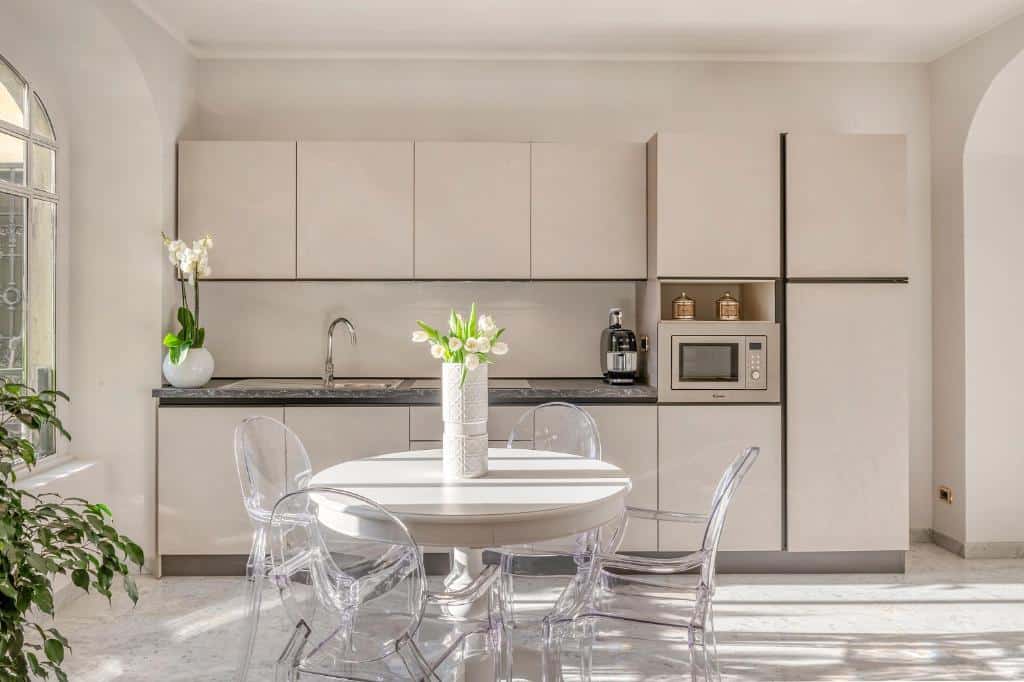 Cozinha do Imperiale Suites Milano com uma mesa redonda com cadeiras transparentes, há um vaso de plantas sob a mesa, para representar airbnb em Milão