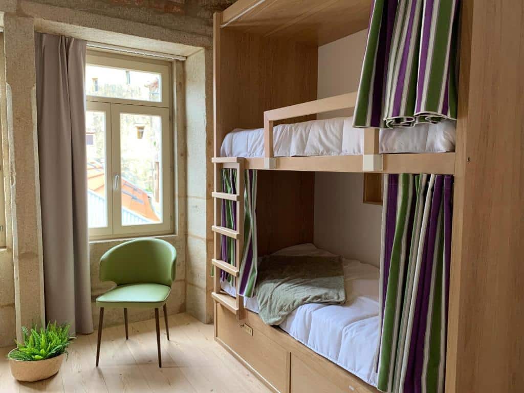 Quarto compartilhado do Lost Inn Porto Hostel com uma cama de beliche do lado direito e uma cadeira verde do lado esquerdo.