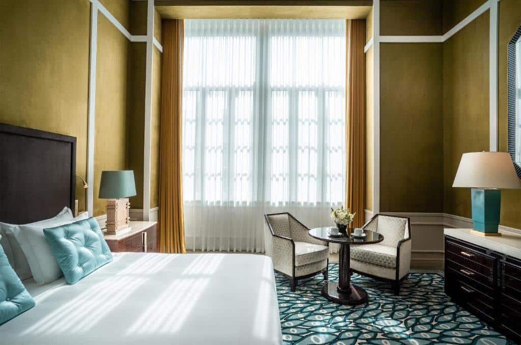 Quarto do Maison Albar Hotels Le Monumental Palace com cama de casal do lado esquerdo e em frente a cama uma cômoda com luminária. Representa hotéis românticos no Porto.