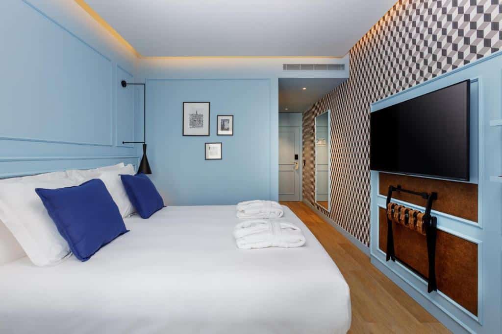 Quarto do Mercure Porto Centro Aliados com cama de casal do lado esquerdo e do lado esquerdo da cama uma pequena mesa de trabalho com cadeira. Representa hotéis bem localizados no Porto.