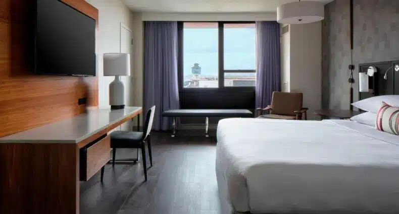 quarto do New York LaGuardia Airport Marriot com uma cama de casal à direita, uma televisão de tela plana preso à esquerda na parede, em frente a cama, e uma janela ao fundo com vista para a torre de controle do aeroporto La Guardia