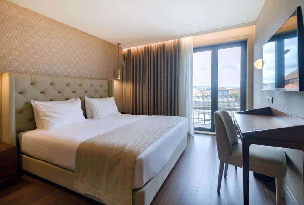 Quarto do Oca Oriental Porto Hotel com cama de casal do lado esquerdo em frente a cama uma mesa de trabalho com TV acima da mesa de trabalho pendurado na parede. Representa hotéis baratos no Porto.