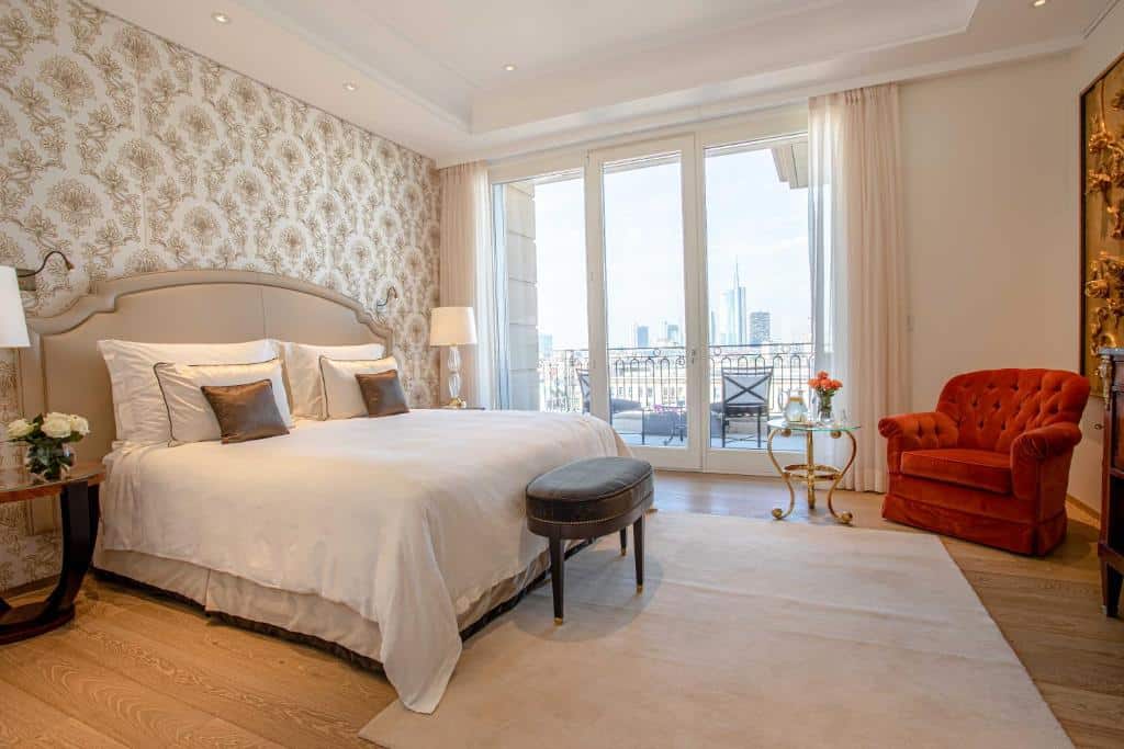 Quarto do Palazzo Parigi Hotel & Grand Spa - LHW com uma varanda ampla com duas cadeiras e uma pequena mesinha, uma cama de casal, uma poltrona acolchoada vermelha e um tapete bege