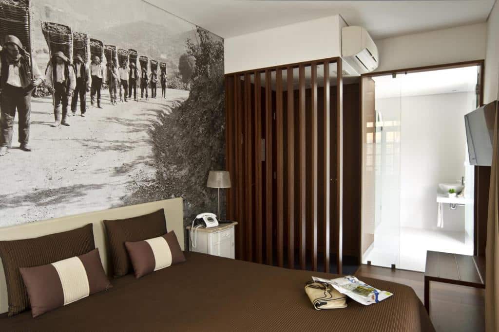 Quarto do Ribeira do Porto Hotel com cama de casal do lado esquerdo um pouco a frente da cama uma cômoda com TV pendurada na parede. Representa hotéis baratos no Porto.