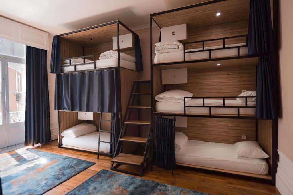 Quarto do Rosalma Hostel com duas beliches uma em cada lado com três camas cada e uma escada no meio delas. Representa hostels no Porto.