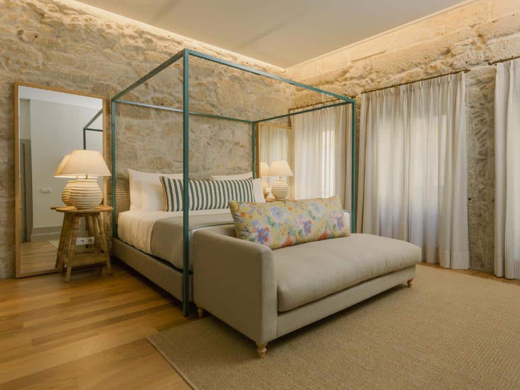 Quarto do Saboaria com cama de casal do lado esquerdo, duas cômodas ao lado da cama com luminária e no pé da cama um sofá. Representa hotéis no centro do Porto