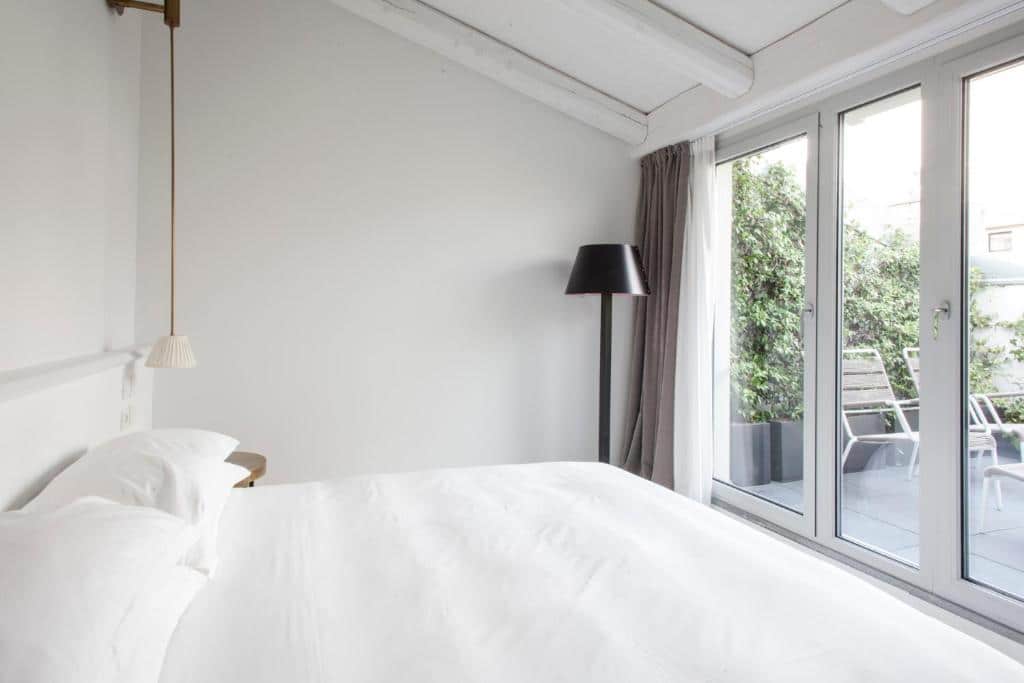 Quarto do Senato Hotel Milano com uma terraço com portas de vidro, cama de casal, abajur de chão e uma mesinha de cabeceira, todo o ambiente é branco