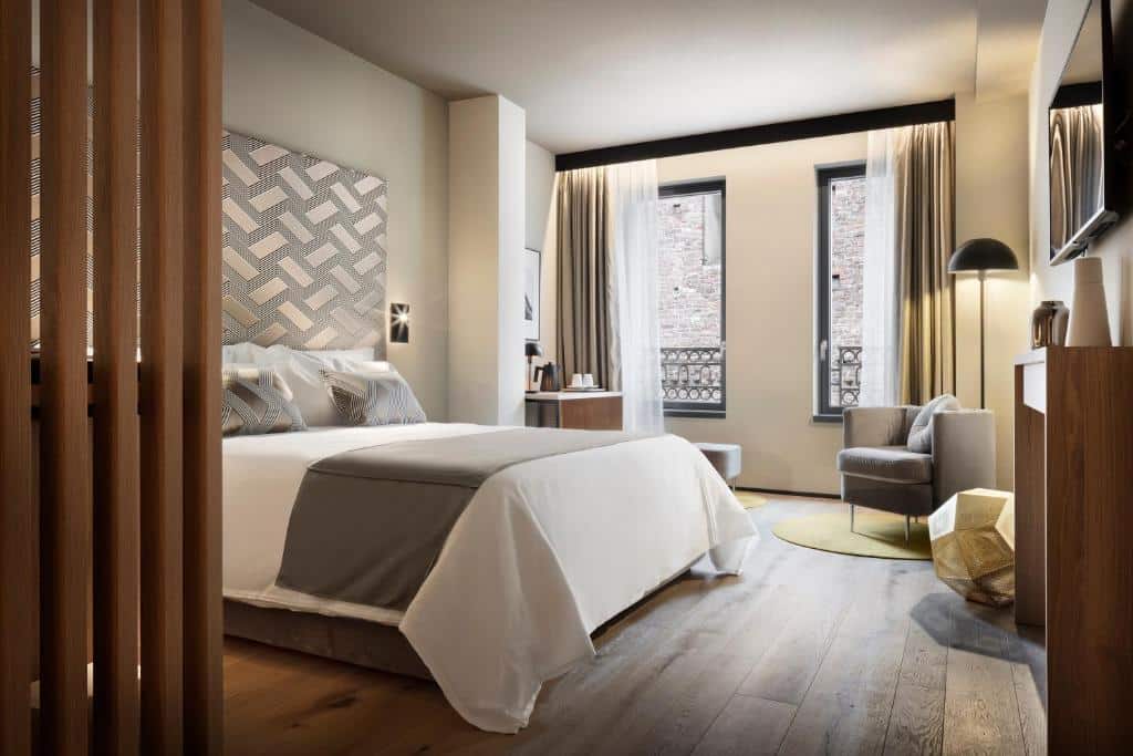 Quarto do Speronari Suites com duas janelas com cortinas, piso que imita madeira, uma cama de casal, uma mesinha com cafeteira e xícaras, uma poltrona e um abajur de chão, para representar hotéis boutique em Milão