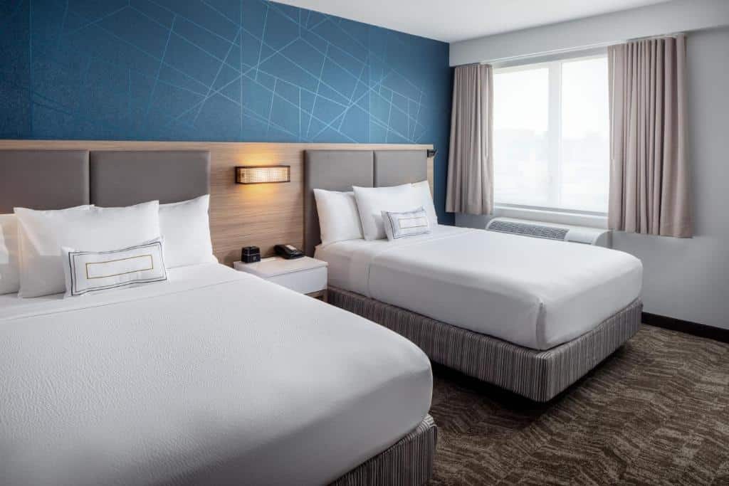 quarto duplo do SpringHill Suites by Marriott perto do aeroporto JFK em Nova York com duas camas queen, dispostas lado a lado com lençóis brancos e uma parede estilizada em azul