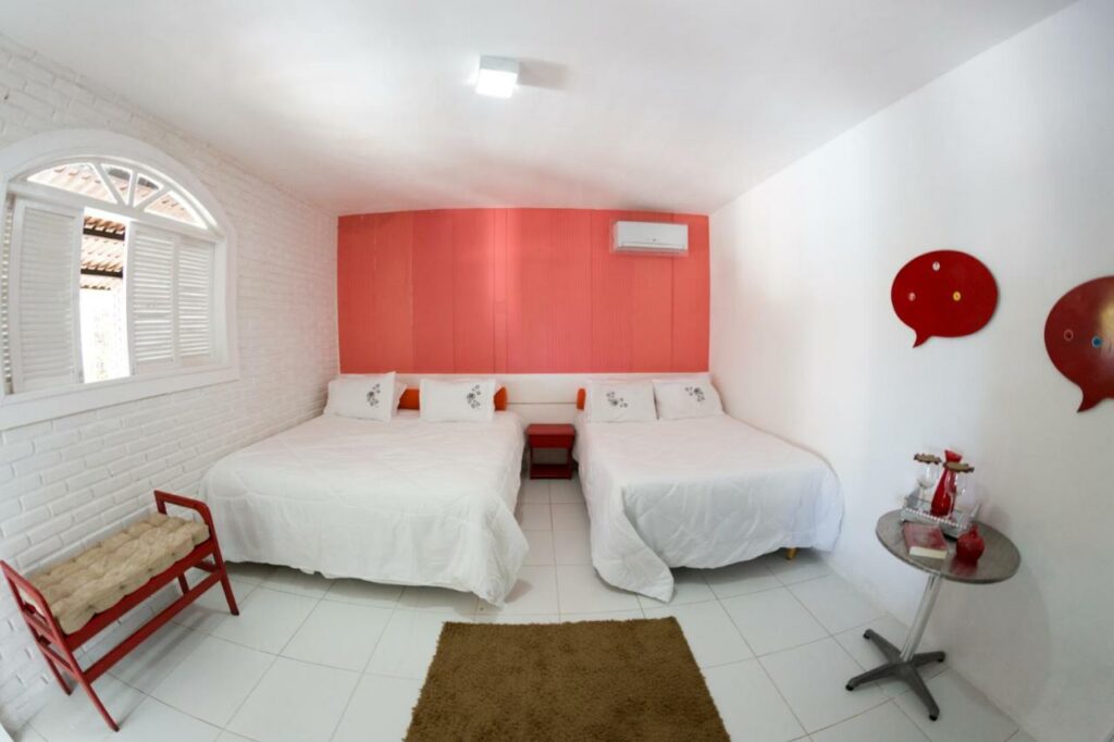 Quarto do Rancho da Dóris com duas camas de casal, um recamier, uma mesinha e uma janela. Foto para ilustrar post sobre pousadas em Barra de de São Miguel.