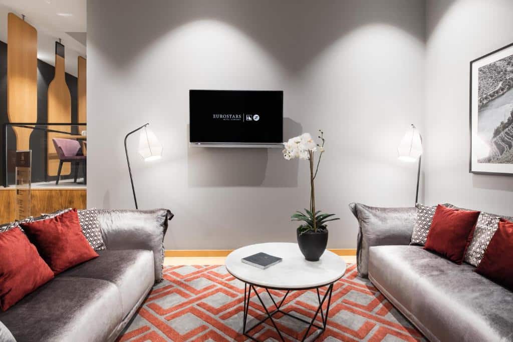 Sala do Eurostars Porto Centro com sofás cinzas de cada lado, uma pequena mesa redonda entre os sofás e uma TV ao meio pendurada na parede.