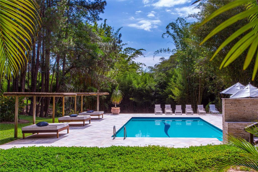 Área externa de resort com piscina, espreguiçadeiras brancas e área verde com árvores em volta.