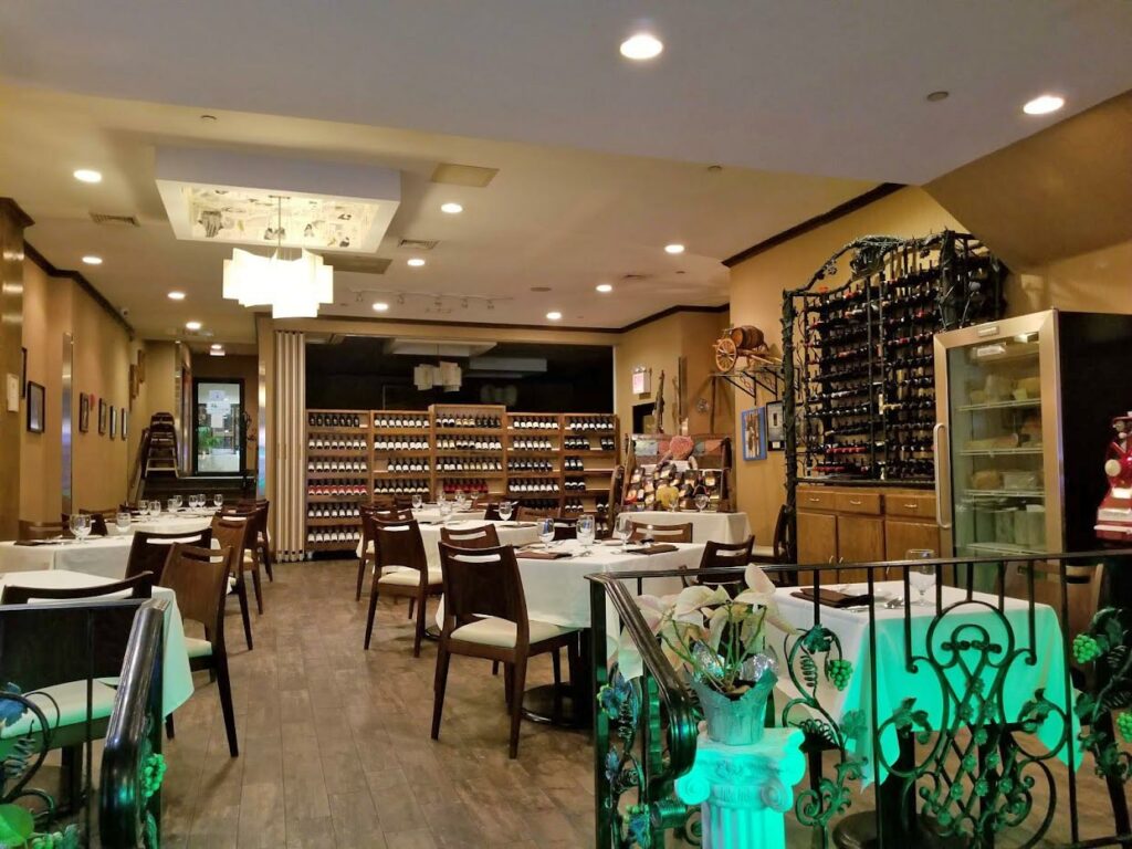 restaurante do Marco LaGuardia Hotel & Suites com várias mesas quadradas de madeiras, acompanhadas por quatro cadeiras em cada, com uma toalha branca por cima, além de guardanapos de tecido marrom e copos de vidro.
