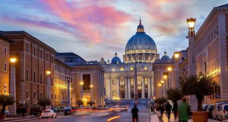 vista do Hotel Della Conciliazione, um dos hotéis para brasileiros em Roma, em que é possível ver o domo da Praça de São Pedro ao entardecer, com luzinhas e pessoas caminhando