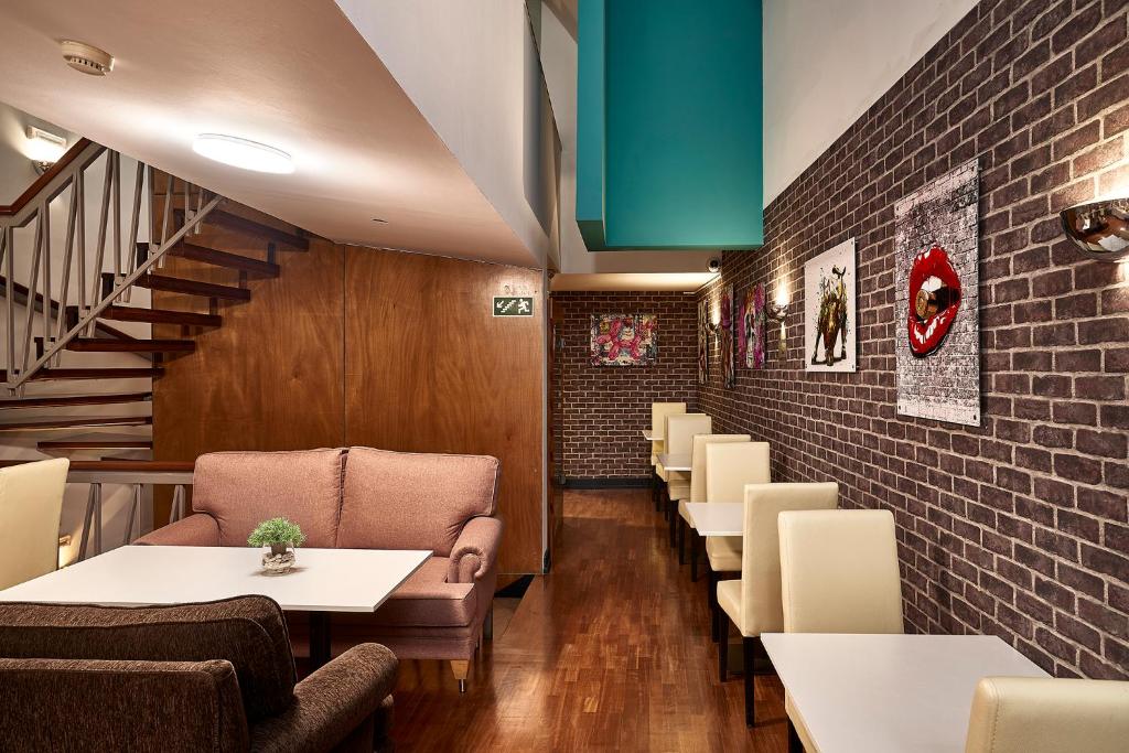 Área para refeições em hotel com paredes de tijolinho, quadros decorativos, mesas brancas com cadeiras brancas para duas pessoas ao lado direito e mesa branca com sofás para quatro pessoas ao lado esquerdo.