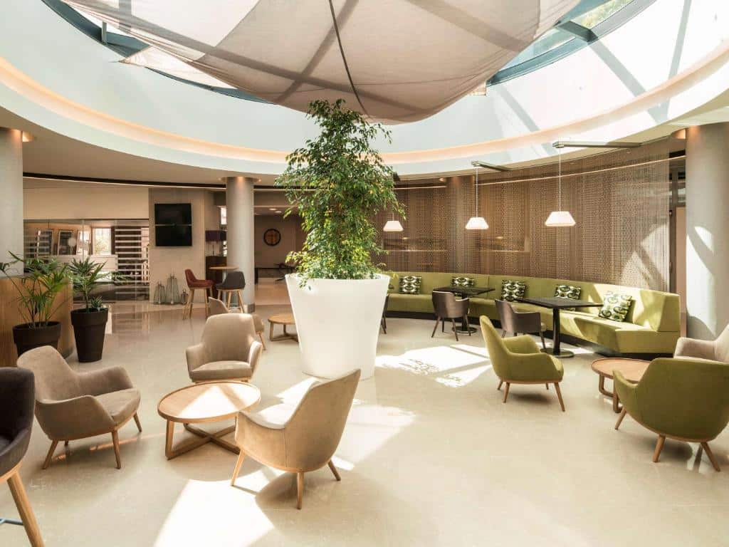 Sala de estar do Hotel Mercure Porto Gaia com cadeiras e poltronas no ambiente e no centro um vaso grande com uma árvore.