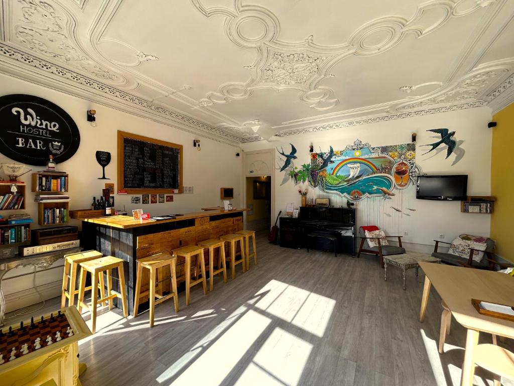 Sala de estar do Porto Wine Hostel com balcão do lado esquerdo da imagem com bancos de madeira e do lado direito da imagem cadeiras e uma TV.