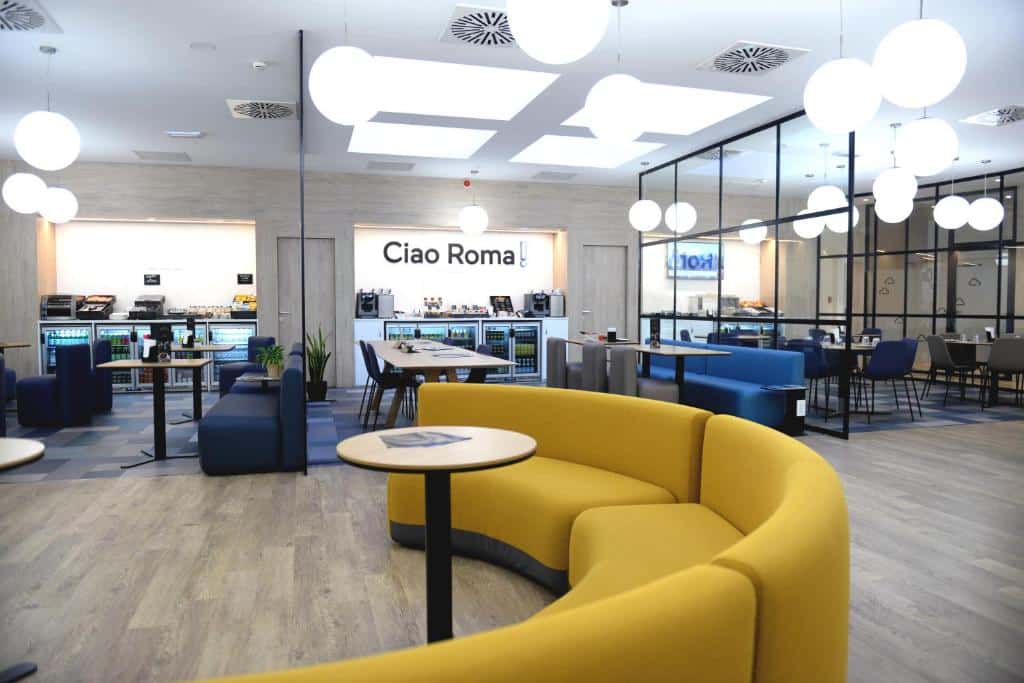 salão do Air Rooms Rome Airport by HelloSky com sofás amarelos e azuis em um ambiente de refeições e também com máquinas de lanches