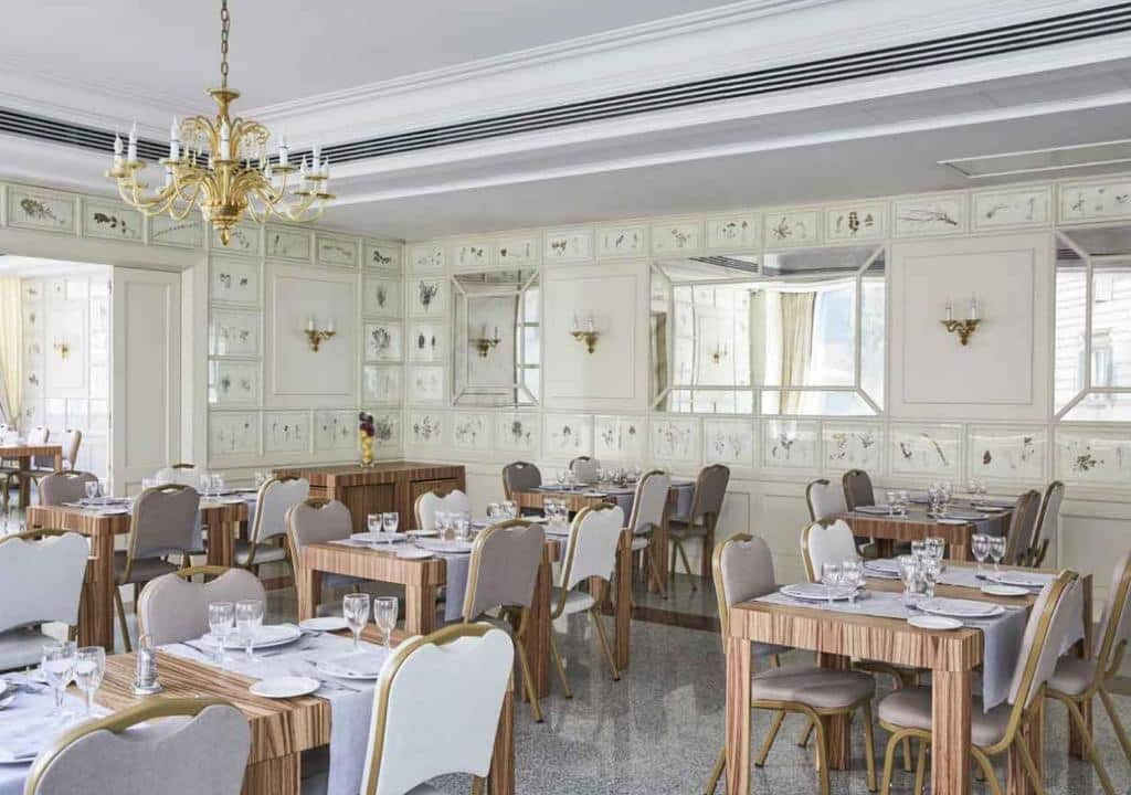 salão do FH55 Grand Hotel Palatino com mesas e cadeiras de madeira cobertas com toalhas brancas, lustre dourado no teto e paredes internas trabalhadas brancas