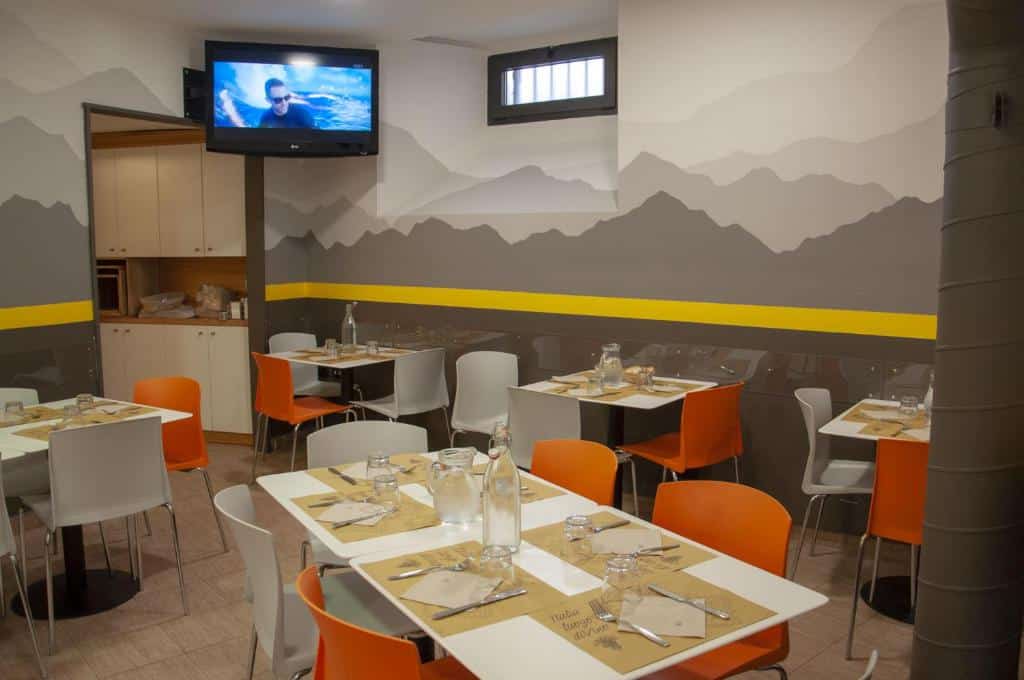 salão do Roma Scout Center com tv e mesas com cadeiras laranjas simples, mas confortáveis