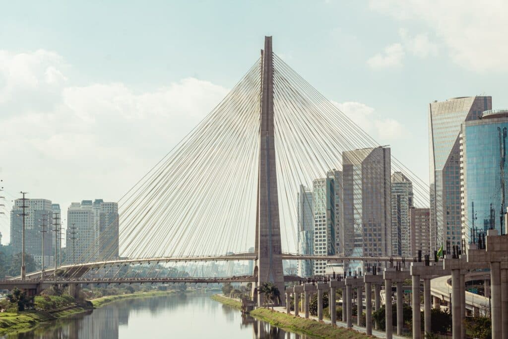 Imagem da Ponte Octávio Frias de Oliveira, ou Ponte Estaiada, em São Paulo. Ao redor da construção, vemos os inúmeros edifícios e prédios da capital.