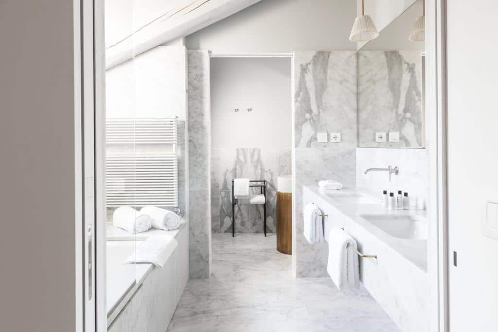 Banheiro amplo do Senato Hotel Milano com uma banheira de hidro, uma pia com duas cubas, um espelho, e ganchos com toalhas brancas penduradas