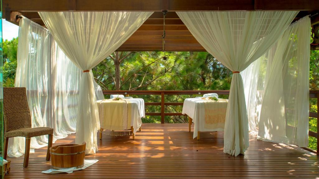 Espaço para massagem feito com deck de madeira com cortinas brancas, duas macas com lençóis brancos e cadeira de madeira ao lado.