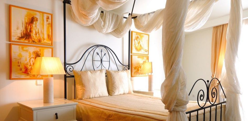Quarto com decoração clássica, cama de casal com lenços em volta e quadros e luminárias ao lado da cama. Imagem para ilustrar o post hotéis em Aveiro.