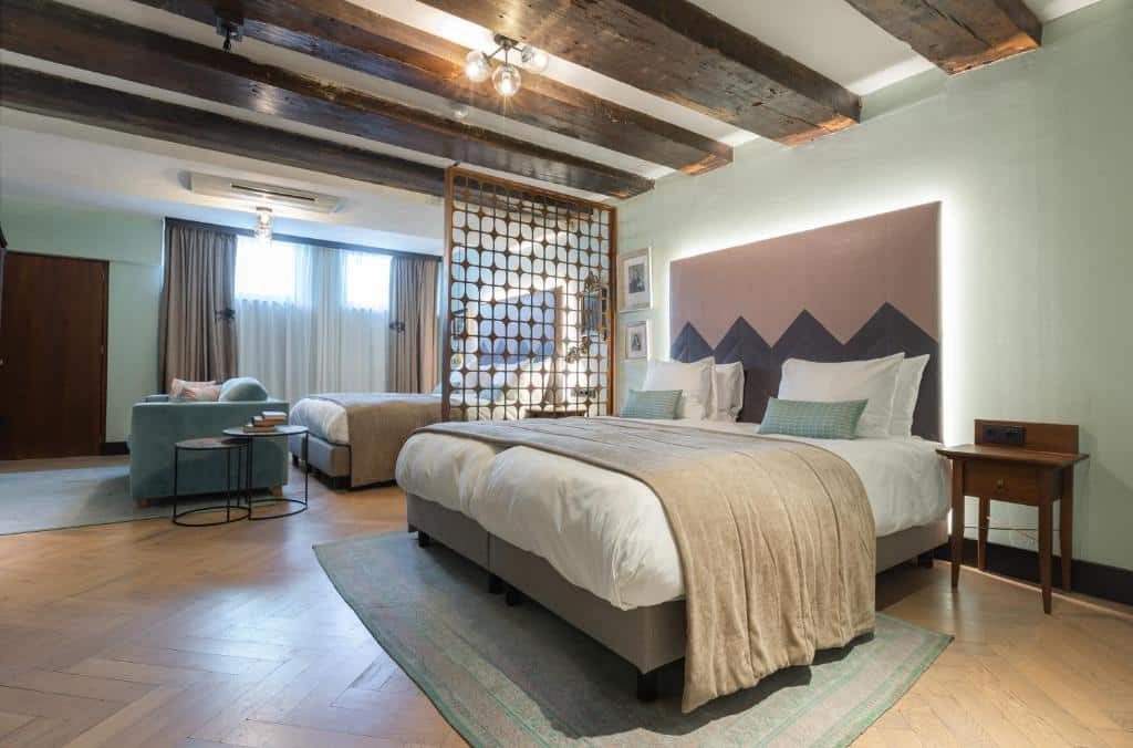Suíte Semi do The Hendrick's Hotel, de 45 m², com duas camas de casal grandes, separadas por uma parede de madeira ripada, e uma sala de estar com sofá. Imagem para ilustrar o post de hotéis para família em Amsterdam