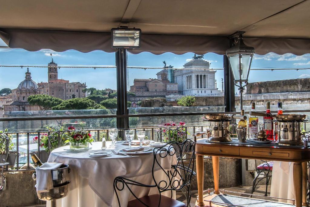 terraço coberto do Hotel Forum com vista para o Fórum Romano, mesa e cadeiras de ferro, com sucos e bebidas em uma mesinha de madeira