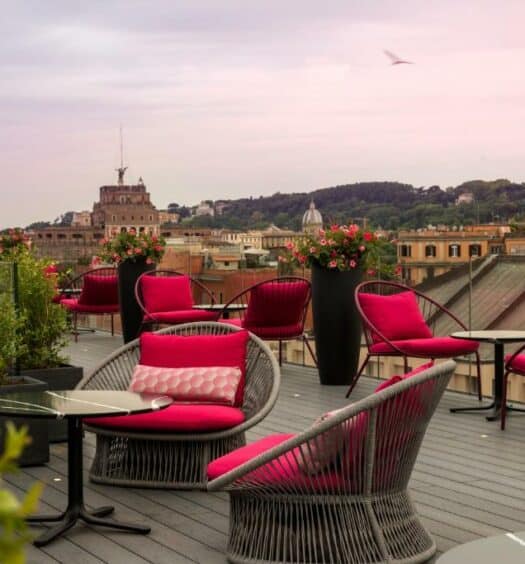 terraço do Orazio Palace Hotel, um dos hotéis perto do Vaticano em Roma, com mesinhas e poltronas trançados com almofadas vermelhas e vista para a cidade