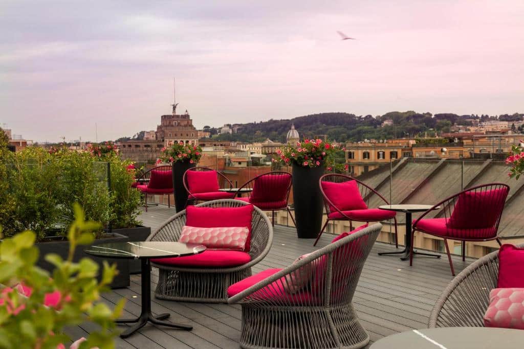 terraço do Orazio Palace Hotel, um dos hotéis perto do Vaticano em Roma, com mesinhas e poltronas trançados com almofadas vermelhas e vista para a cidade