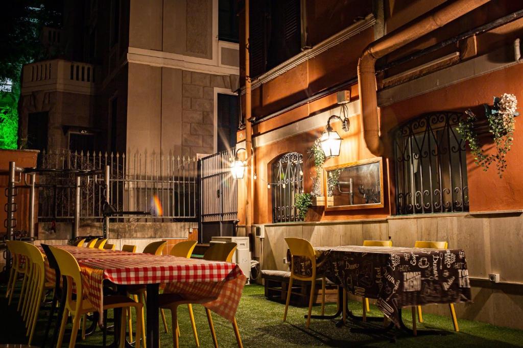 varanda do Free Hostels Roma com mesas e cadeiras com toalhas xadrez vermelhas, luminárias e o ambiente está à noite com grama e portinhas de madeira