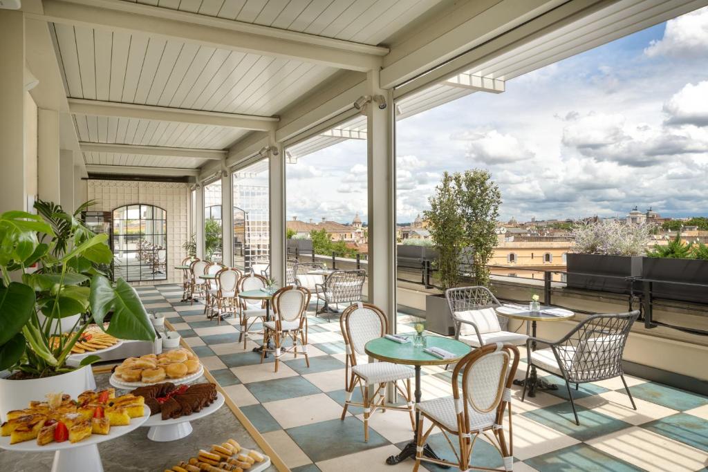 varanda do UNAHOTELS Trastevere Roma, com mesinhas e cadeiras ao estilo clássico em tons de azul claro, com café da manhã posto e ambiente coberto com vista para a cidade