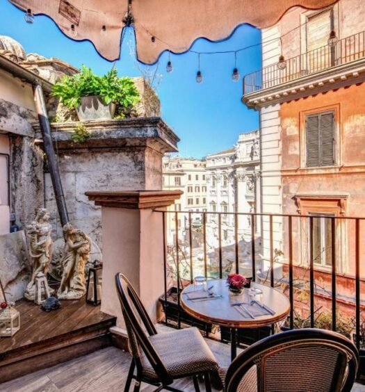 vista direta da praça no Relais Fontana Di Trevi Hotel, um dos hotéis perto da Fontana di Trevi em Roma, com mesinha e cadeiras, esculturas de um lado e vista total da fonte