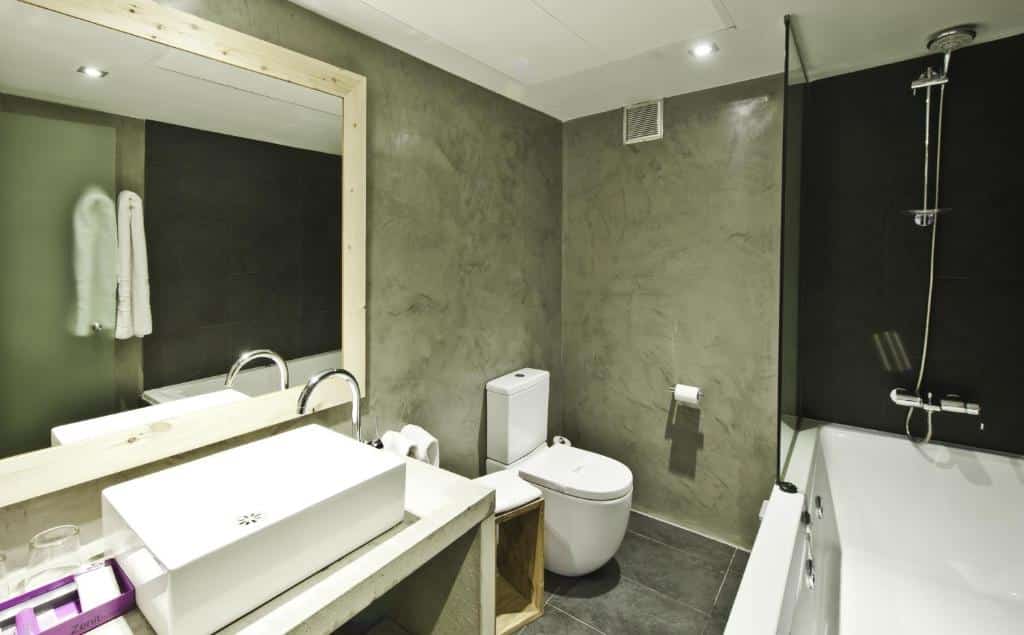 Banheiro do Zenit Abeba. A pia com espelho encara uma banheira com box e tem uma privada ao lado.