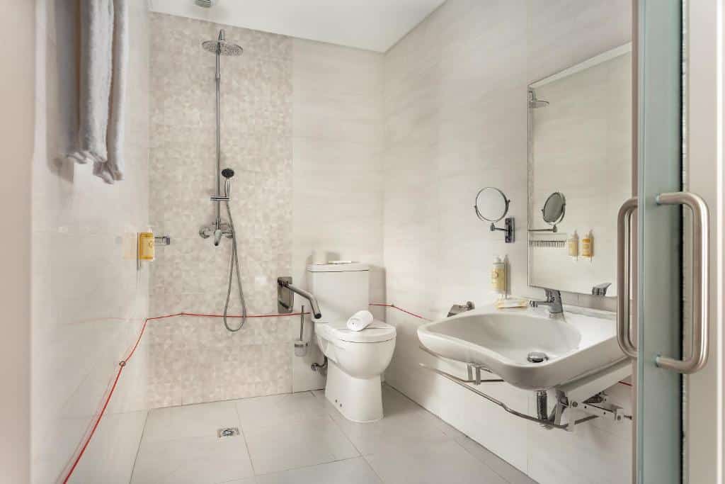 Banheiro adaptado do Empire Marquês Hotel com barras de apoio, box sem vidro, cordão de emergência e pia mais baixa sem um móvel embaixo dela, para representar hotéis baratos em Lisboa