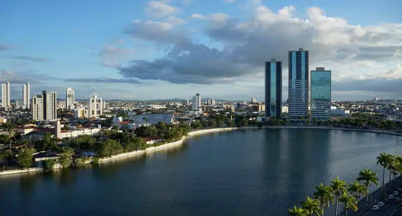 Vista do Açude Velho, em Campina Grande. Um lafo no meio, ao redor palmeiras e árvores. No canto direito do lago, uma avenida, no lado esquerdo várias casas e prédios. Foto para ilustrar post sobre pousadas em Campina Grande.