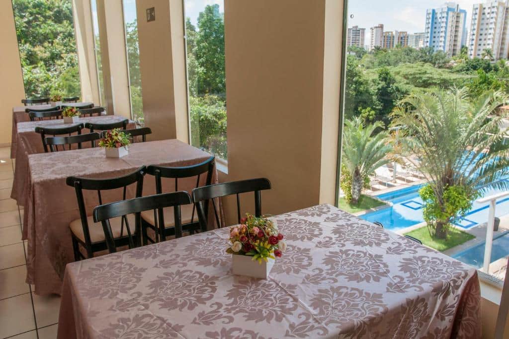 Parte do hotel Águas do Paranoá que tem algumas mesas para as pessoas fazerem suas refeições. Na foto mostra quatro mesas com cadeiras e janelas de vidro com vista para a piscina do hotel, ilustrando post Hotéis em Caldas Novas.