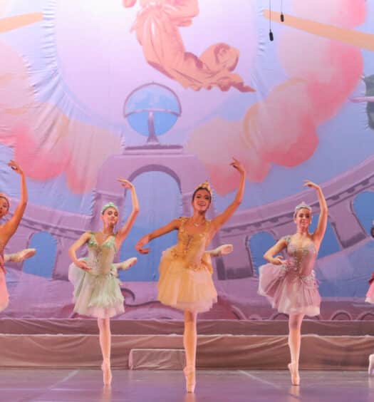 grupo de bailarinas mulheres dançando na ponta dos pés enquanto usam tutus coloridos em tons pastéis e sorriem para o público
