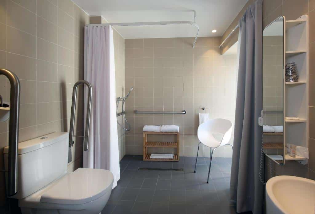 Banheiro adaptado do Hotel Convento do Salvador com barras de apoio nas laterais do vaso sanitário, box sem vidro e com local para sentar-se, para representar hotéis em Lisboa