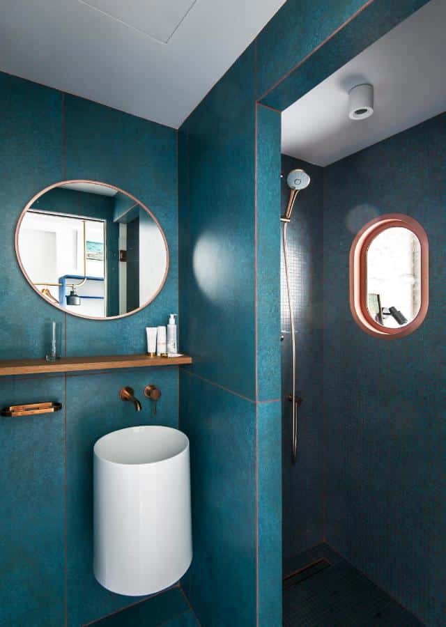 Banheiro do Boutique Hotel Miramar. No lado direito o chuveiro com uma pequena janela. No lado esquerdo um espelho redondo, uma prateleira e uma pia redonda.