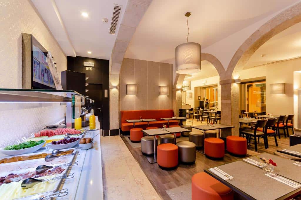 Salão de refeições do Hotel Santa Justa com mesinhas de madeira com sofás e bufes coloridos, do lado esquerdo há um amplo balcão com opções de café da manhã