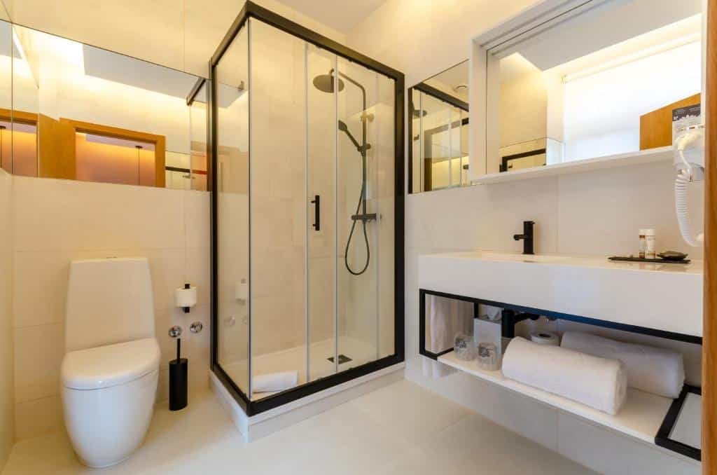 Banheiro do Rossio Plaza Hotel com uma box de vidro, ao lado dele há um vaso sanitário e um espelho, do lado esquerdo há uma cuba ampla com uma pia e, no mesmo móvel, há toalhas brancas disponíveis